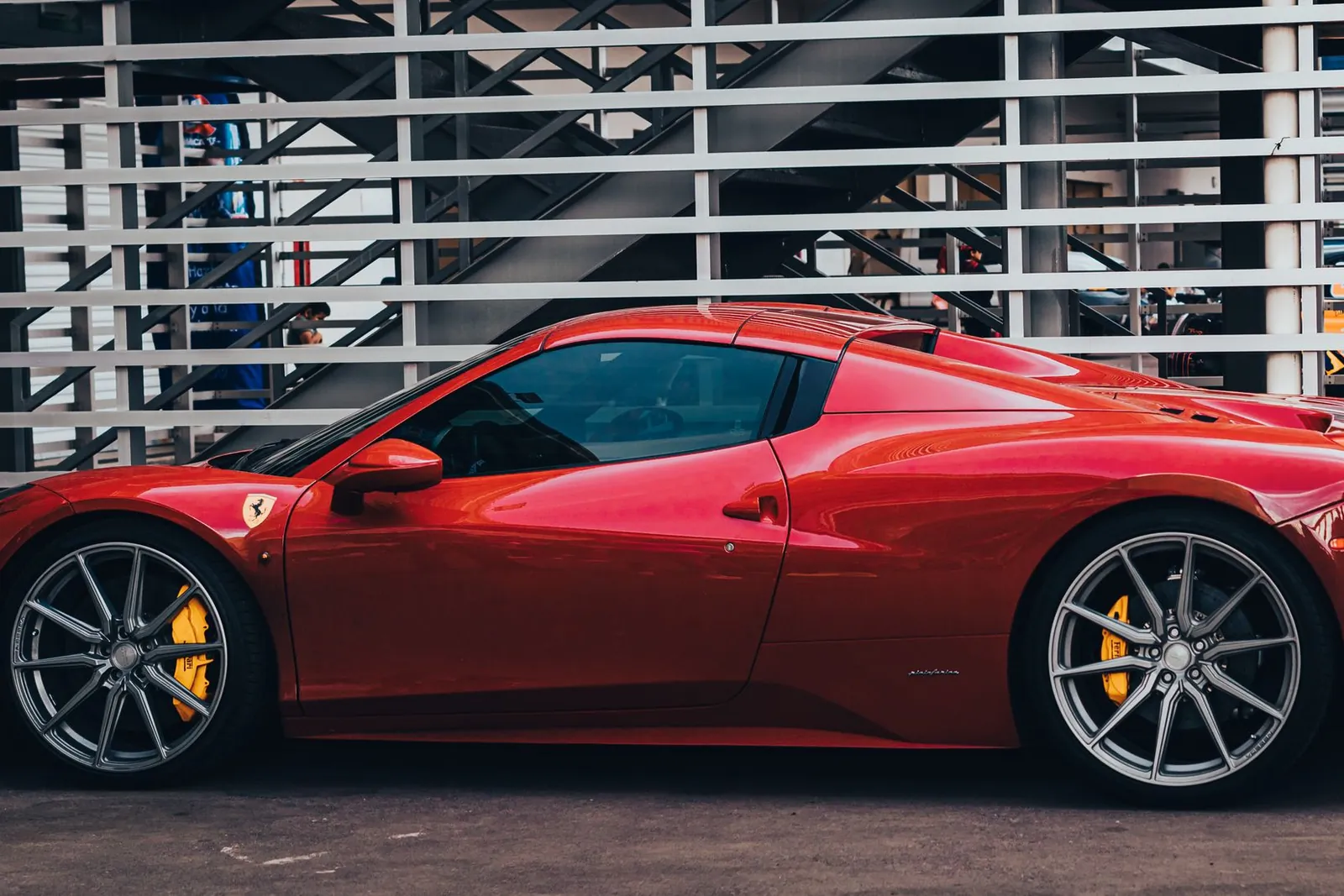 A red Ferrari parked side-on in front of a slatted white facade.